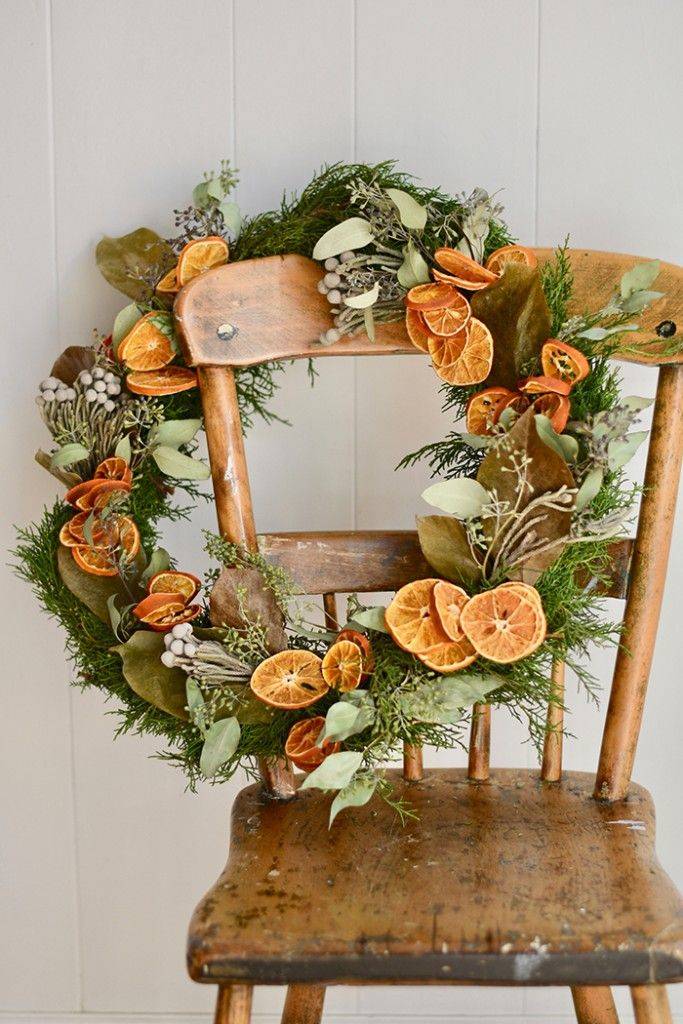 Natural, real greenery Christmas wreath with dried oranges hanging on vintage chair white background