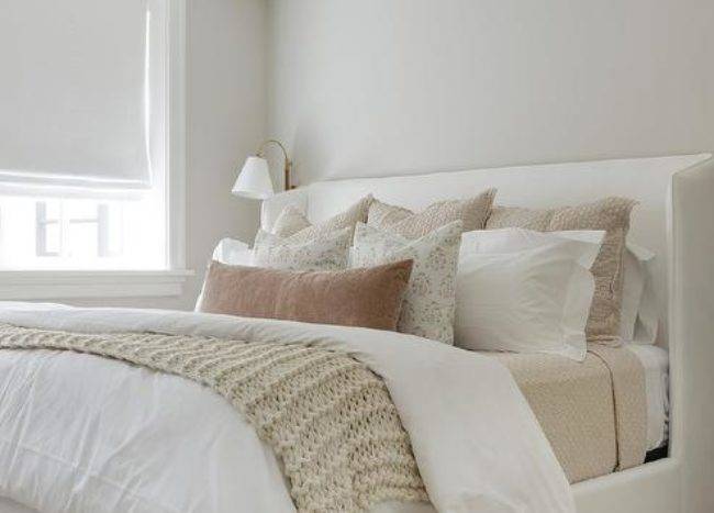 A white upholstered wingback bed is complemented with tan and brown layered pillows placed on white and tan bedding.