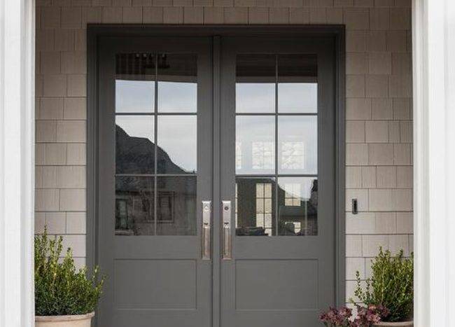 Styled front porch features layered welcome mats in front of gray and glass front door finished with potted plants.