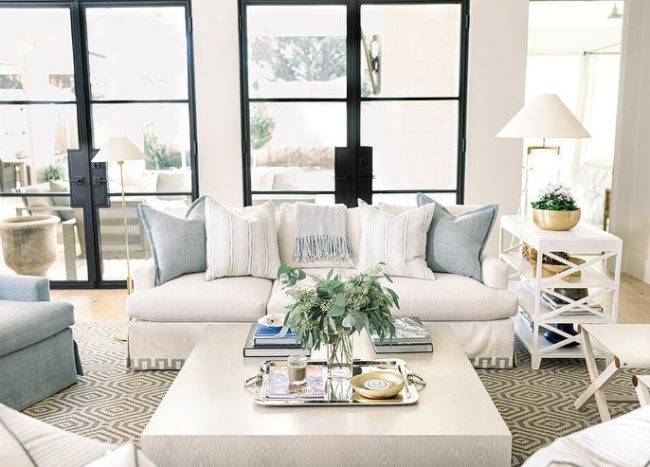 Light gray oak block coffee table on a hexagon jute rug is centered between a white Greek key sofa and various accent chairs in a transitional living room design.