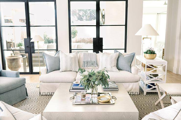 Light gray oak block coffee table on a hexagon jute rug is centered between a white Greek key sofa and various accent chairs in a transitional living room design.