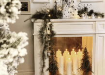 white fireplace at christmas time with white pillar candles inside decorative small christmas trees and white ceramic trees on mantle