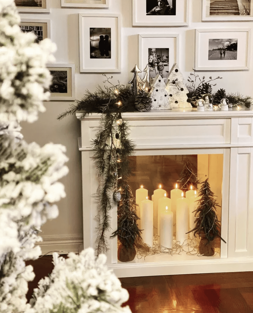 white fireplace at christmas time with white pillar candles inside decorative small christmas trees and white ceramic trees on mantle