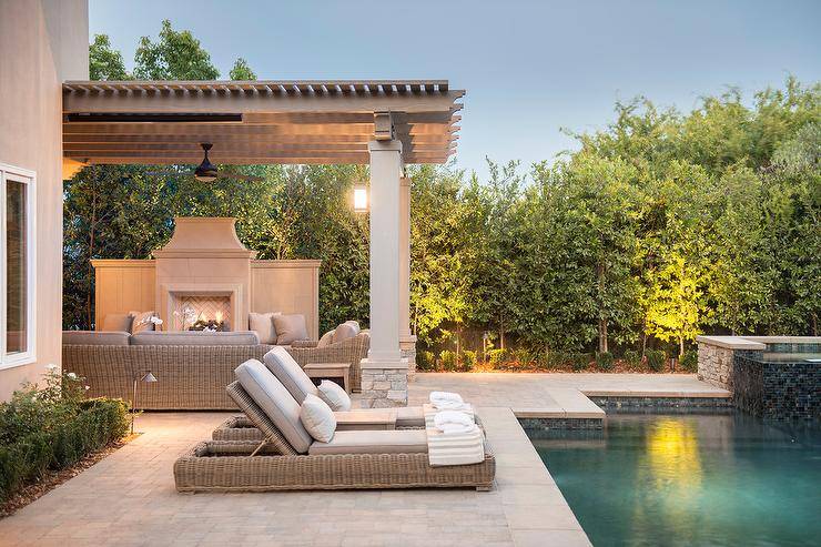 Chic outdoor space features a gray pergola placed over a stone fireplace accented with a herringbone firebox facing a wicker sofa and chairs.