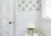 Lovely bathroom features upper walls clad in blue and green floral wallpaper and lower walls clad in white subway tiles lined with a white bamboo tray table atop a marble herringbone floor next to a multi paneled door.