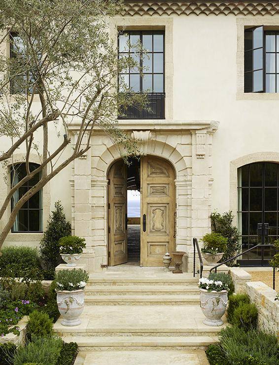 French provincial home exterior features double front carved wood doors and a Juliet balcony beside glass and steel windows.