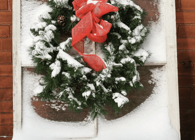 evergreen wreath with red bow hanging on snow covered window