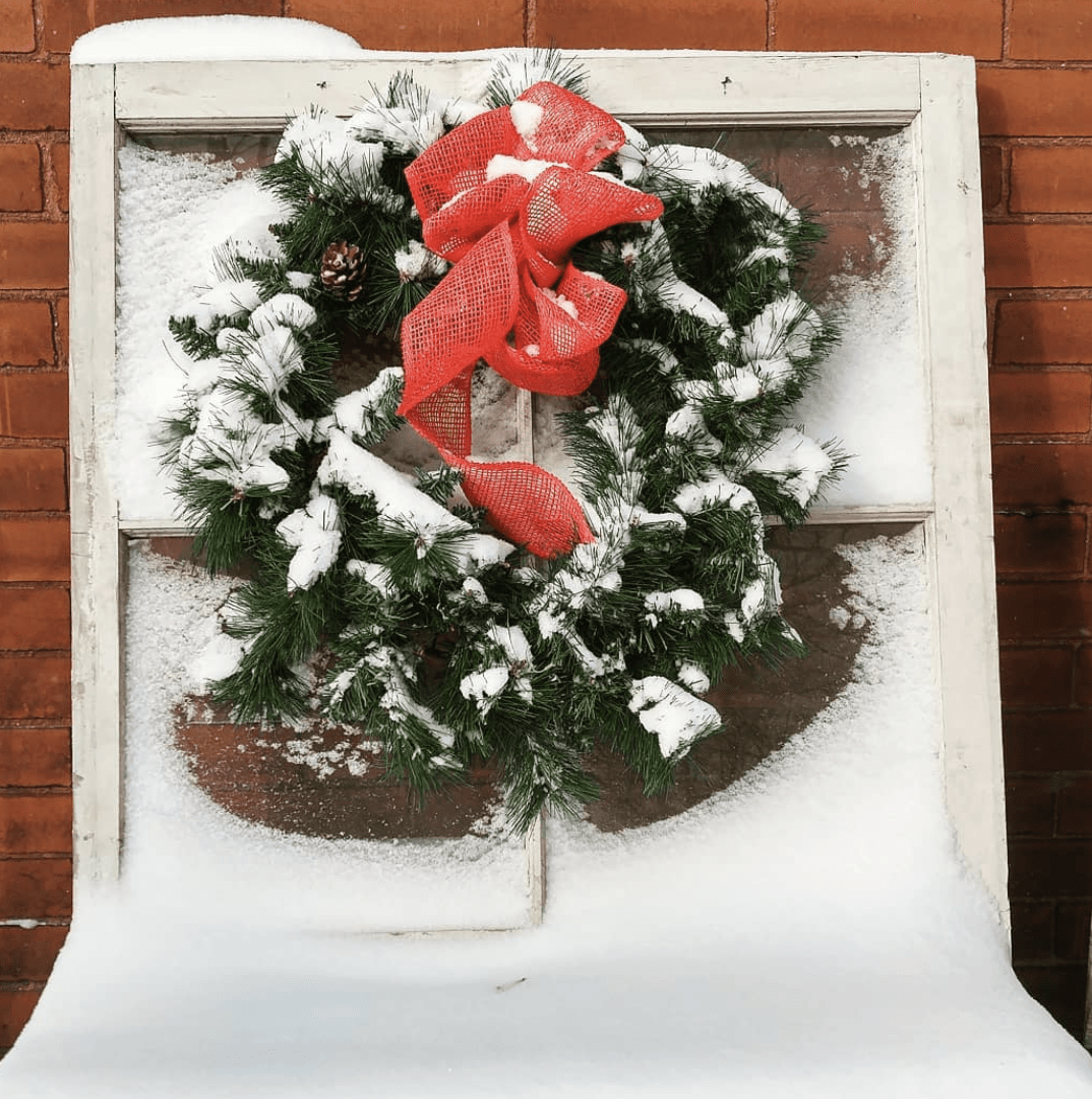 evergreen wreath with red bow hanging on snow covered window