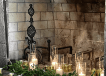 glass hurricane candles in brick fireplace with greenery
