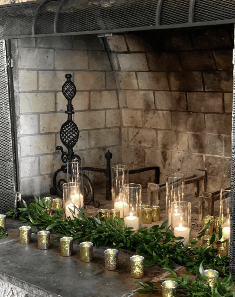 glass hurricane candles in brick fireplace with greenery