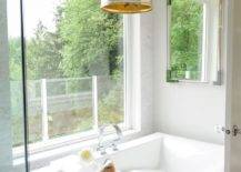 A gold lantern lights a rectangular freestanding bathtub fitted with a lucite bath tray and a chrome deck mount tub filler mounted in front of a picture window.