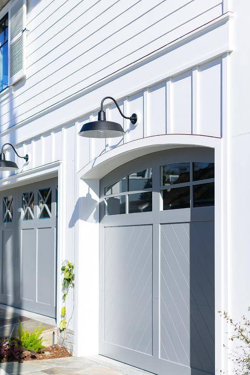 Gray chevron pattern garage doors accent a white cottage home and are lit by black vintage gooseneck lanterns.