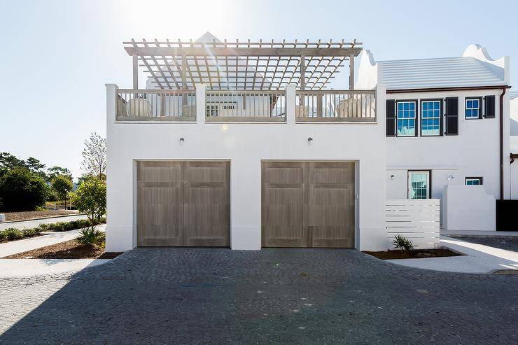 Stunning beach cottage home features gray wash garage doors fitted beneath a deck accented with a gray wash pergola and a gray washed wood railing.