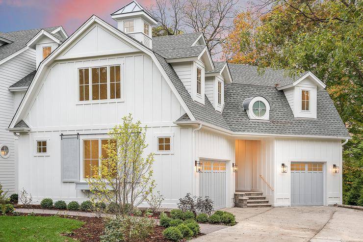 White cottage style house with separate gray garage doors flanked by carriage iron and glass lantern exterior light sconces.