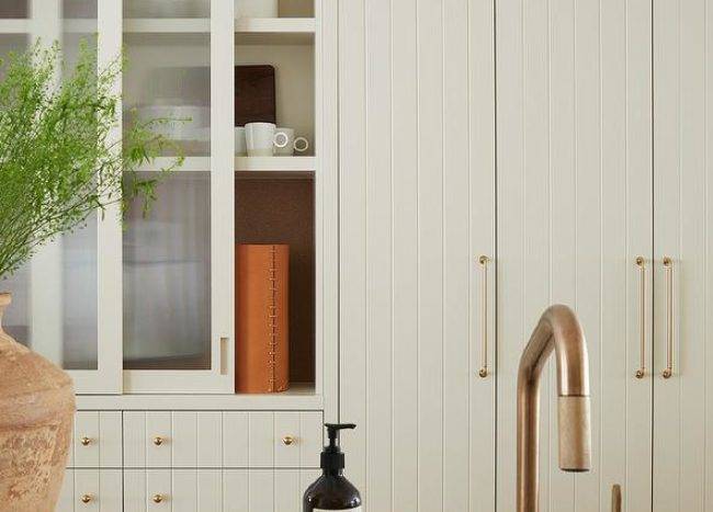 Tall tan plank cabinets donning brass pulls are fixed beside sliding frosted glass cabinet doors stacked over tan plank drawers.