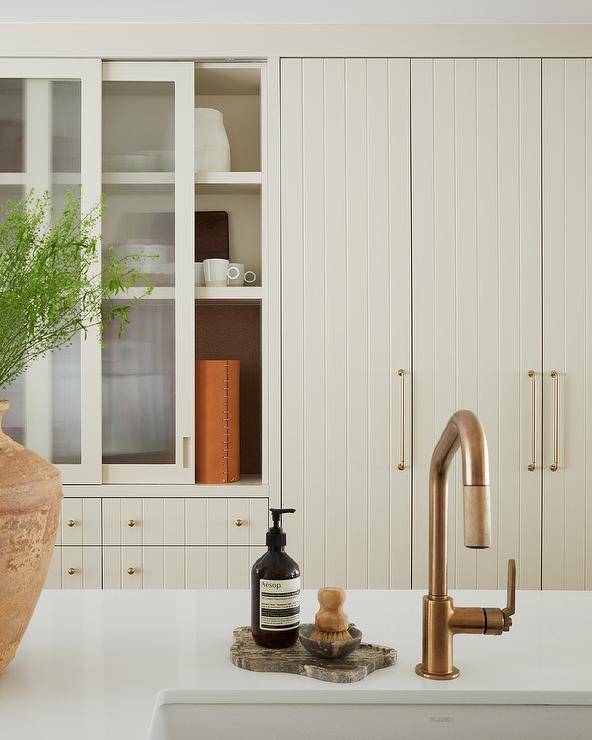 Tall tan plank cabinets donning brass pulls are fixed beside sliding frosted glass cabinet doors stacked over tan plank drawers.