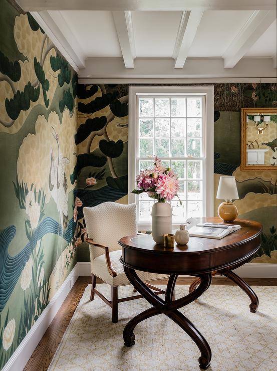 Chic home office is covered in hand-painted wallpaper and furnished with an oval French desk seating white camelback chair on a white and gold trellis rug.