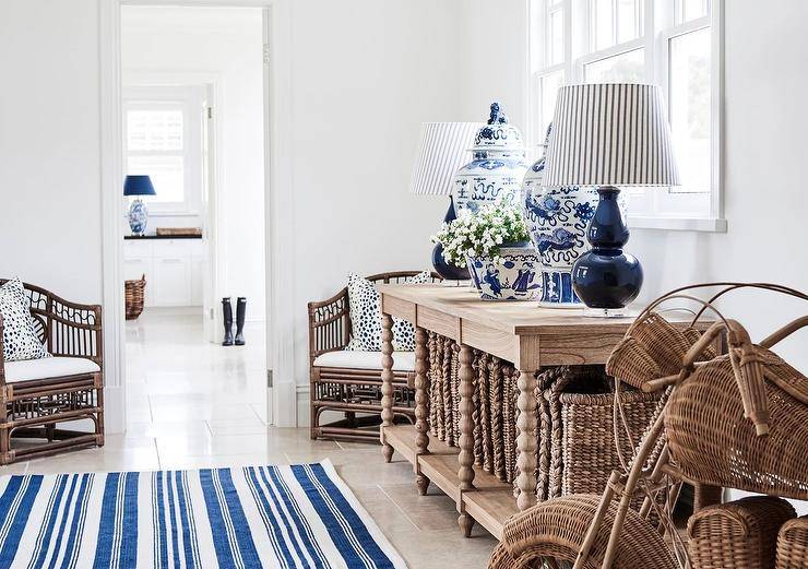 Brown and blue cottage foyer design features navy blue double gourd lamps with blue stripe lamp shades on a brown oak spindle console table with Chinese ginger jars and a blue stripe rug.