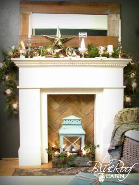 a faux fireplace with a chevron wooden screen, a crate with pinecones, candles, fir brnahces and a blue lantern