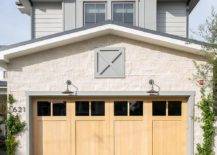 A concrete driveway leads to blond wood garage doors illuminated by vintage barn lanterns.