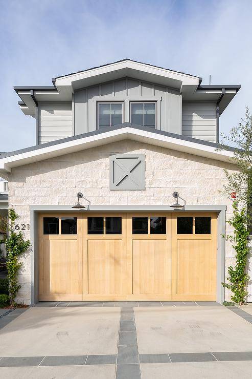 A concrete driveway leads to blond wood garage doors illuminated by vintage barn lanterns.