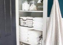 linen closet with open door glass apothecary jar white folded towels hanging towel on hook wicker baskets wire basket on wheels
