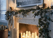 Lit white pillar candles in fireplace with greenery on mantle