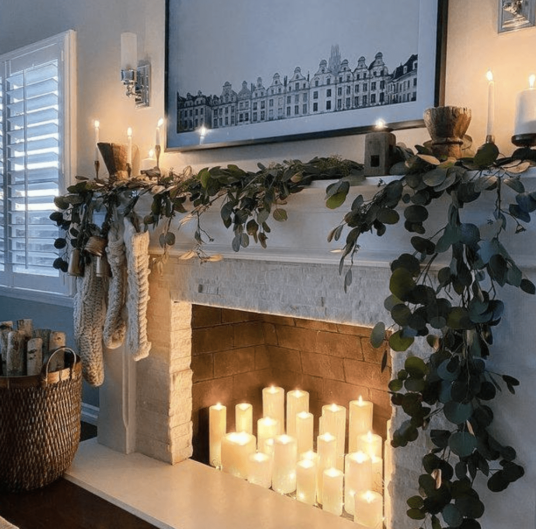 Lit white pillar candles in fireplace with greenery on mantle