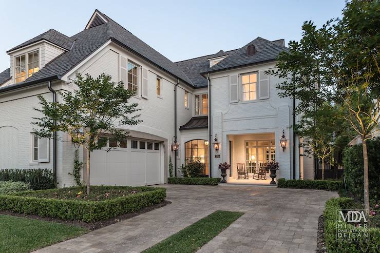 Modern French home features white brick exterior with gray shingles as well as attached his and her garages.