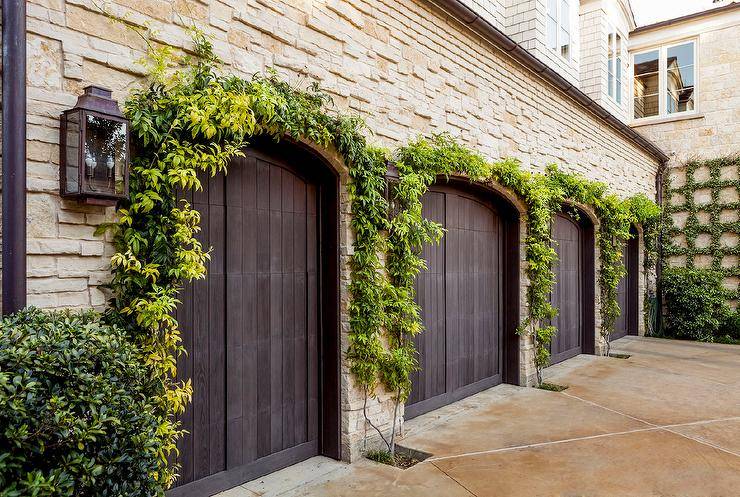 Beautiful home features a four door garage fitted with arched dark stained doors covered in ivy.