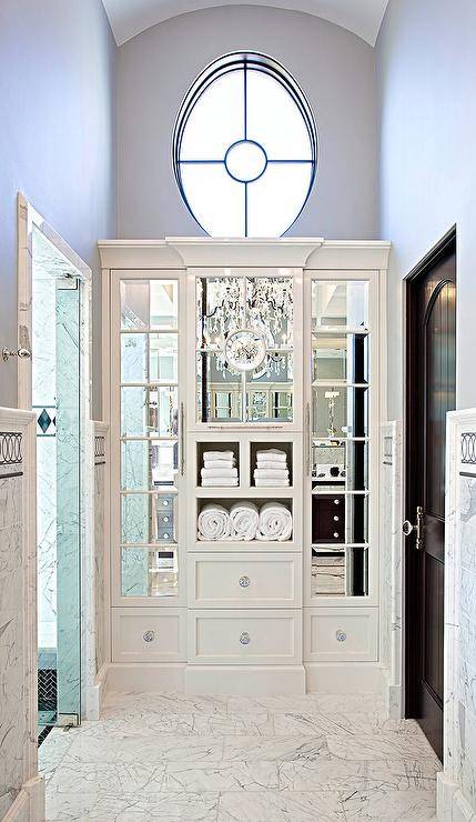 Chic master bathroom boasts a space between a walk in shower and a water closet filled with white built in linen cabinets accented with mirrored doors.