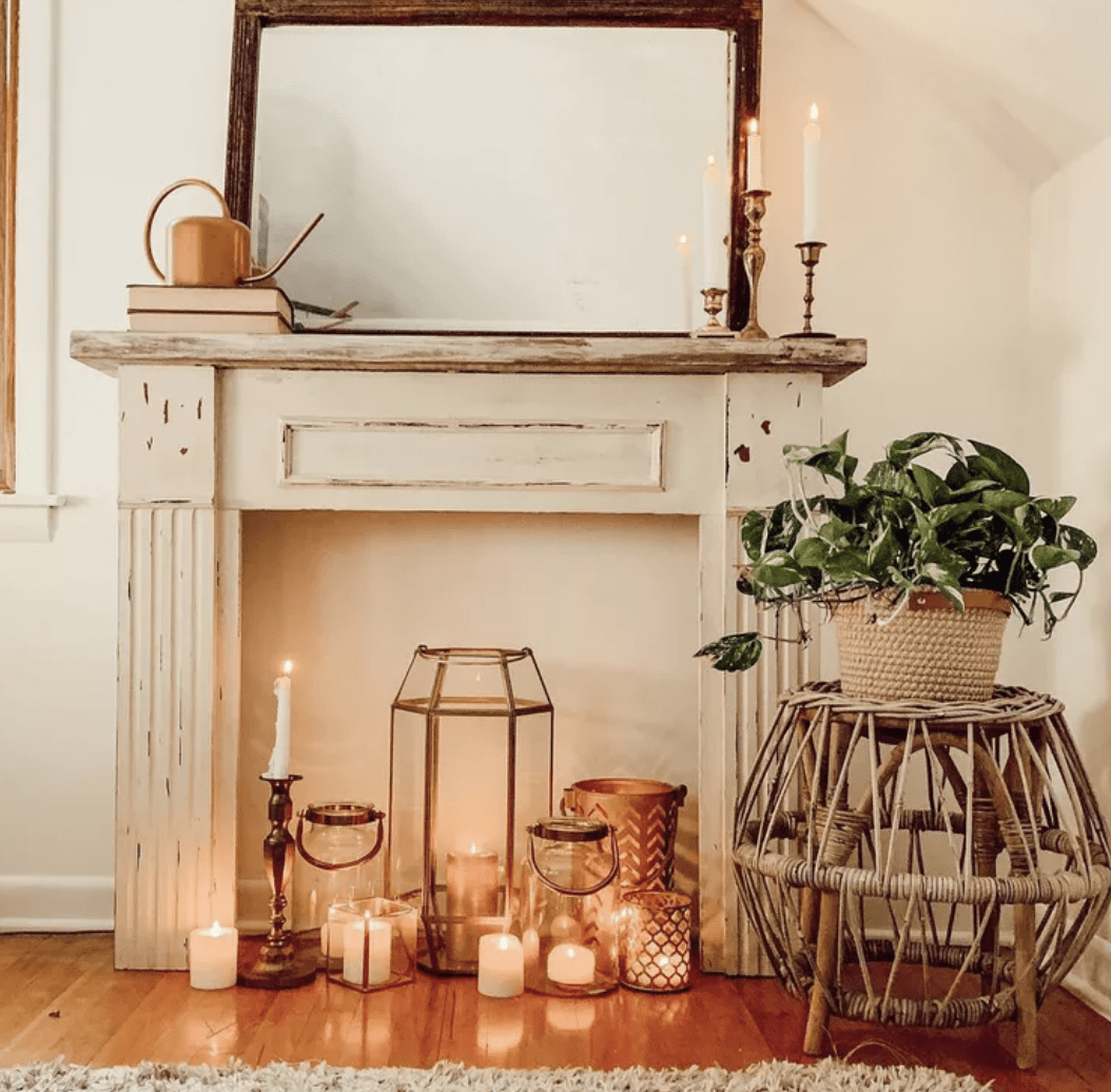 white fireplace mantle with lit candles in front mirror wicker plant stand