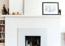 a neutral minimal faux fireplace with lots of various candles inside and very laconic and minimal decor on the mantel