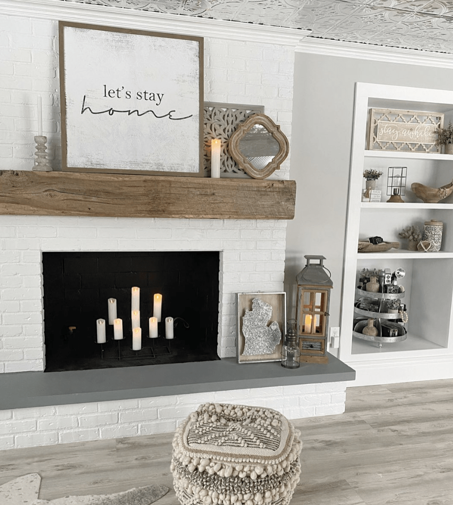 modern boho farmhouse fireplace with candles inside white let's stay home sign on mantle and floor pouf