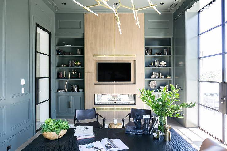 Gray built-in shelves are fixed over gray fireplace cabinets positioned on either side of a gold oak fireplace wall finished with a TV niche located over a double-sided fireplace.