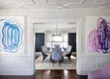 Blue and purple abstract art are hung in a contemporary living room over wainscoting and on either side of a doorway.