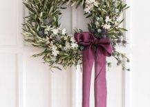olive branch wreath with purple ribbon hanging on white door