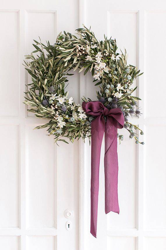 olive branch wreath with purple ribbon hanging on white door