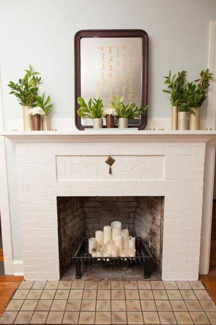 a non-working fireplace of brick, with a metal stand for firewood and pillar candles on it