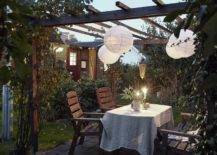 outdoor pergola at night with white hanging paper lanterns outdoor dining area with wood chairs surrounded by greenery