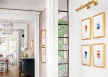 A brass picture light is mounted to a white wall over gold gallery frames.