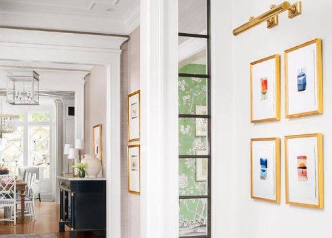 A brass picture light is mounted to a white wall over gold gallery frames.