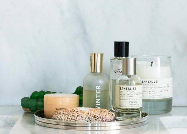 Round perfume tray displaying designer perfumes and skincare essentials on a marble countertop in a transitional bathroom space.