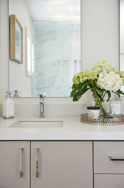 Decorate a bathroom vanity with a round greek key tray to hold decor while adding visual interest atop white quartz countertops.