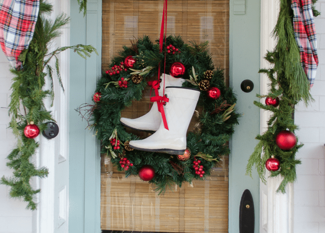 rubber boot christmas wreath hanging on light blue door with greenery and garland with plaid ribbon