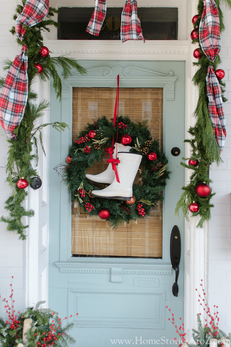 rubber boot christmas wreath hanging on light blue door with greenery and garland with plaid ribbon