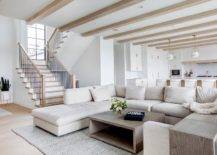 An oatmeal linen sectional sits beneath a ceiling finished with wood beams and on a gray jute rug facing a brown oak coffee table.