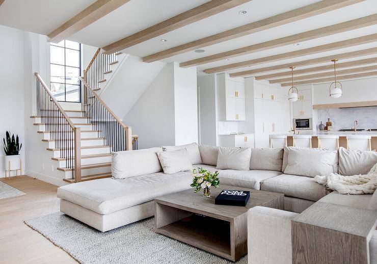 An oatmeal linen sectional sits beneath a ceiling finished with wood beams and on a gray jute rug facing a brown oak coffee table.