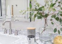 Modern nickel faucets compliment gray marble countertop and Ava vanity mirror. Countertop styling is completed with eucalyptus leaves in a glass vase, decorative candles, and a yellow sponge.