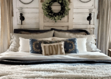 three old vintage doors are used as a bed headboard with a wreath hanging in the middle spiral wall sconces are hanging on the side love pillow fluffy fur throw